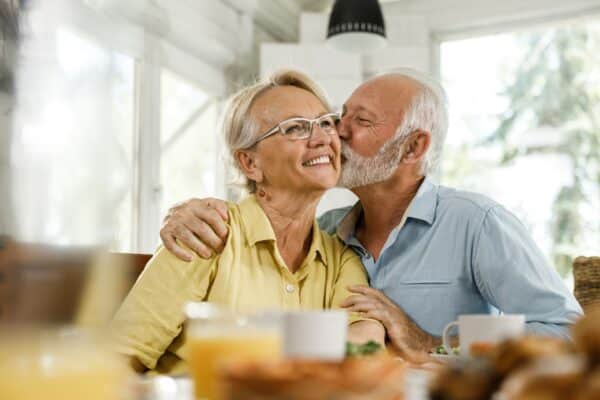 Loving senior man kissing his wife during a meal in dining room.