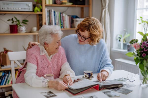 Senior mother with her adult daughter looking at old family pictures at home together.