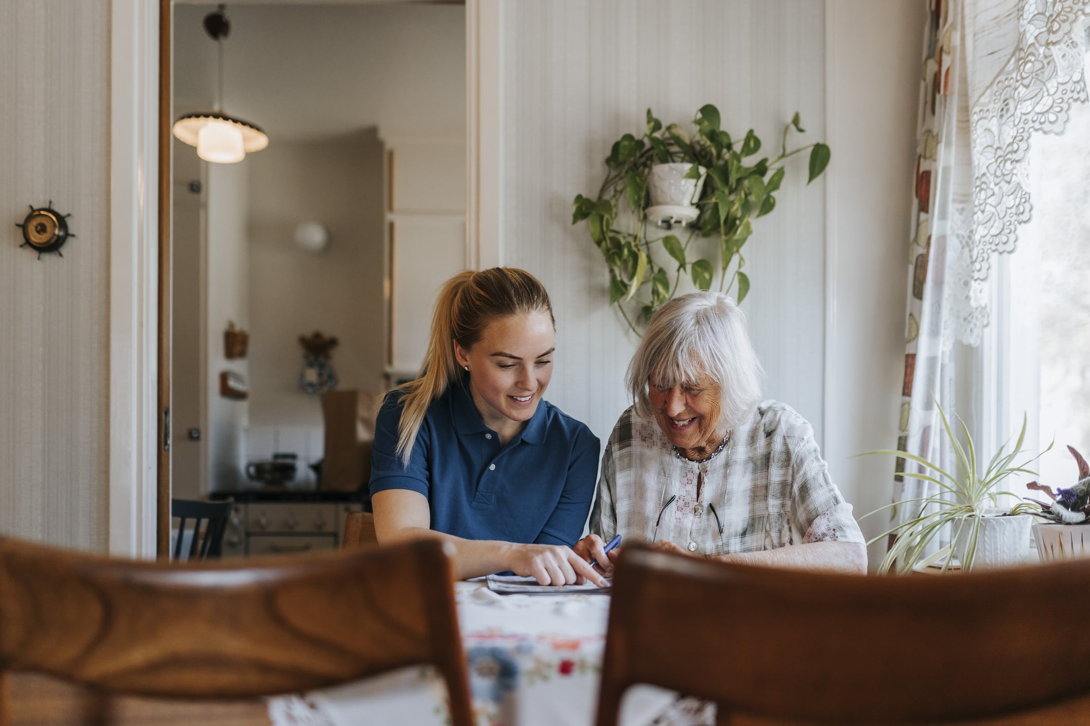 Smiling female caregiver assisting senior woman doing puzzle at home